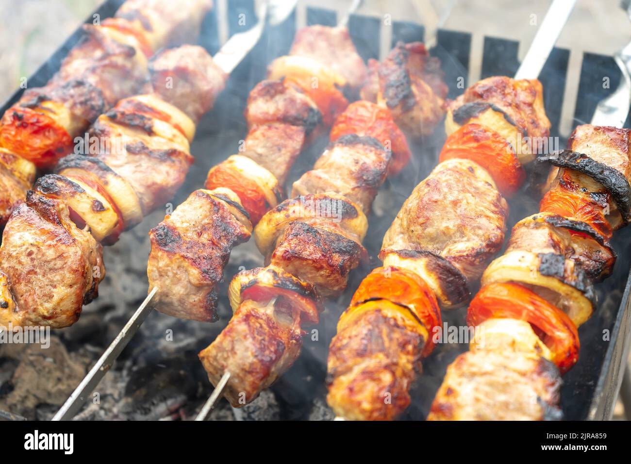 Grilled fried pork meat, pieces of meat on skewers. Process of cooking