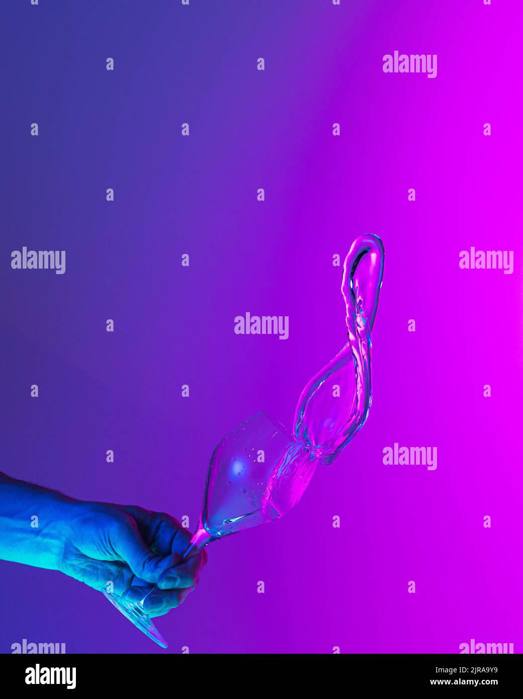 Authentic hand pouring pure water splash from wine or champagne glass over bright bluepink