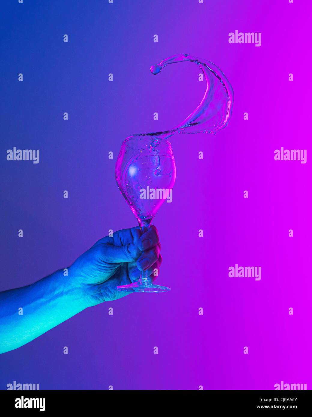 Authentic hand pouring pure water splash from wine or champagne glass over bright bluepink