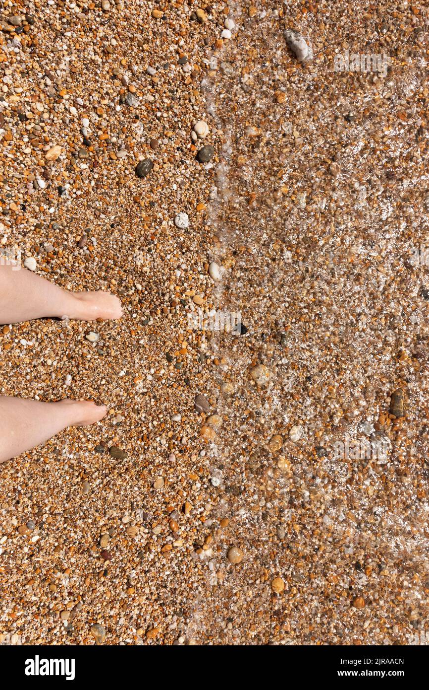 A close up view of a pair of feet buried into the sand-pebbles in the clear ocean water Stock Photo