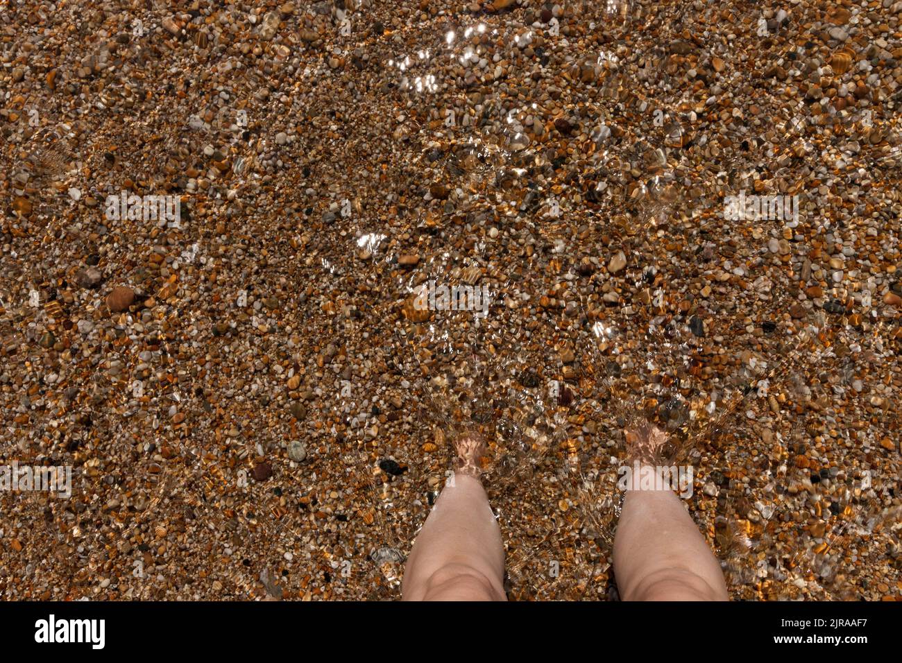 A close up view of a pair of feet buried into the sand-pebbles in the celar ocean water Stock Photo