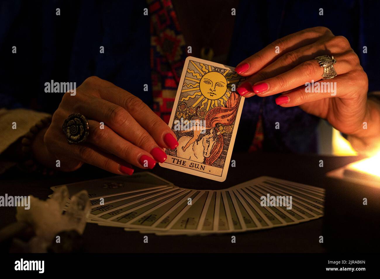 Fortune teller hands showing The Sun tarot card, symbol of positivity, during a reading. Close-up with candle light, moody atmosphere. Stock Photo