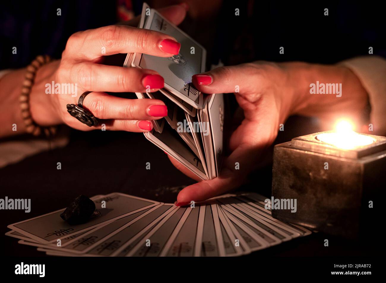 Fortune teller female hands shuffling a deck of tarot cards, during a reading. Close-up with candle light, moody atmosphere. Stock Photo