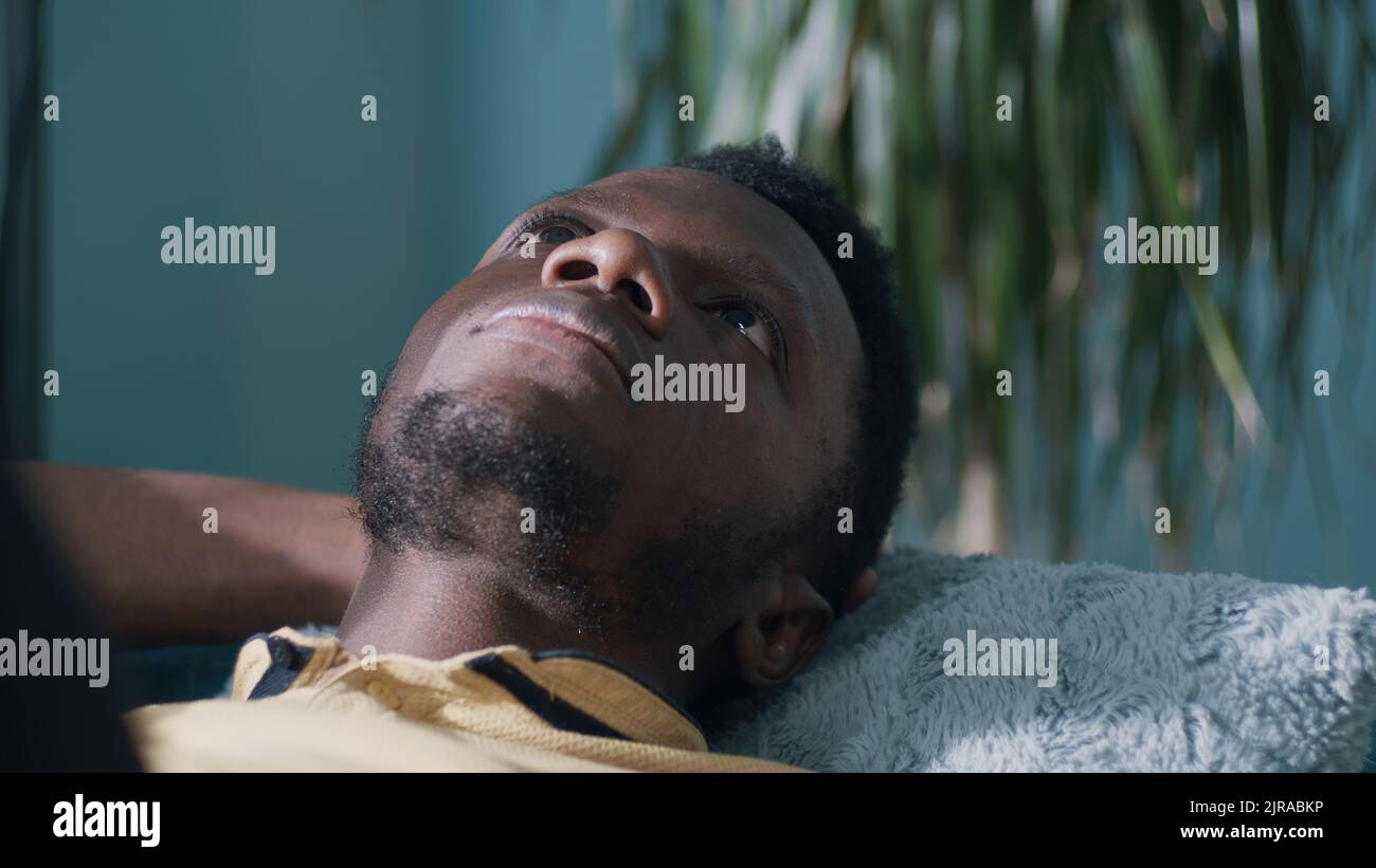 Pensive black guy looking up and thinking while lying on sofa alone at home Stock Photo