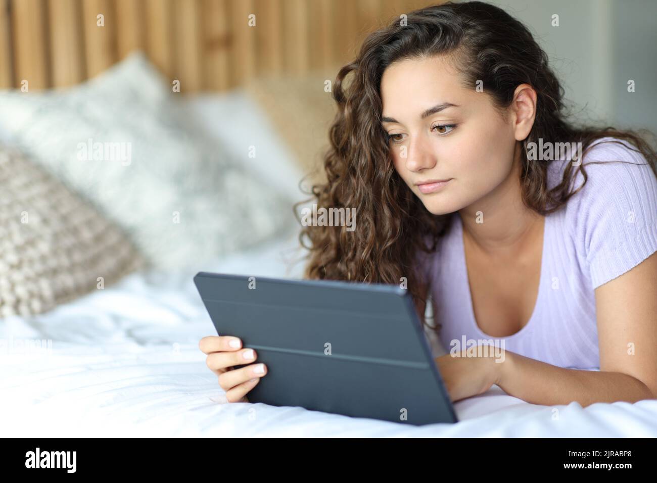 Serious woman using a tablet lying on a bed in the bedroom Stock Photo