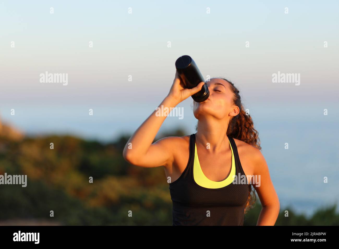 Runner drinking water on the beach at sunset Stock Photo