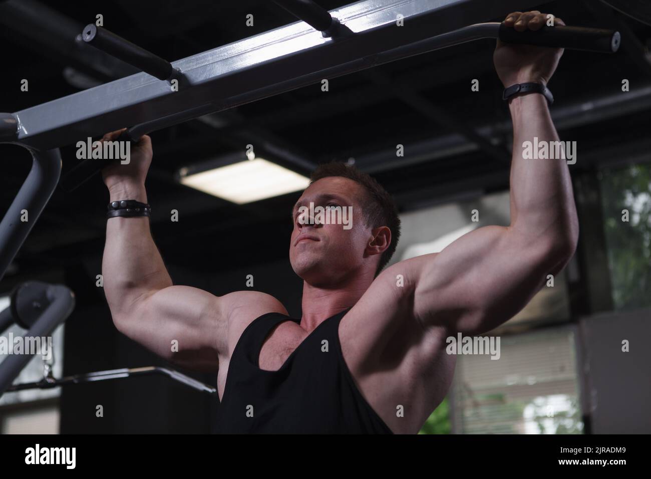 Athletic muscular man exercising at gym, doing pull ups Stock Photo