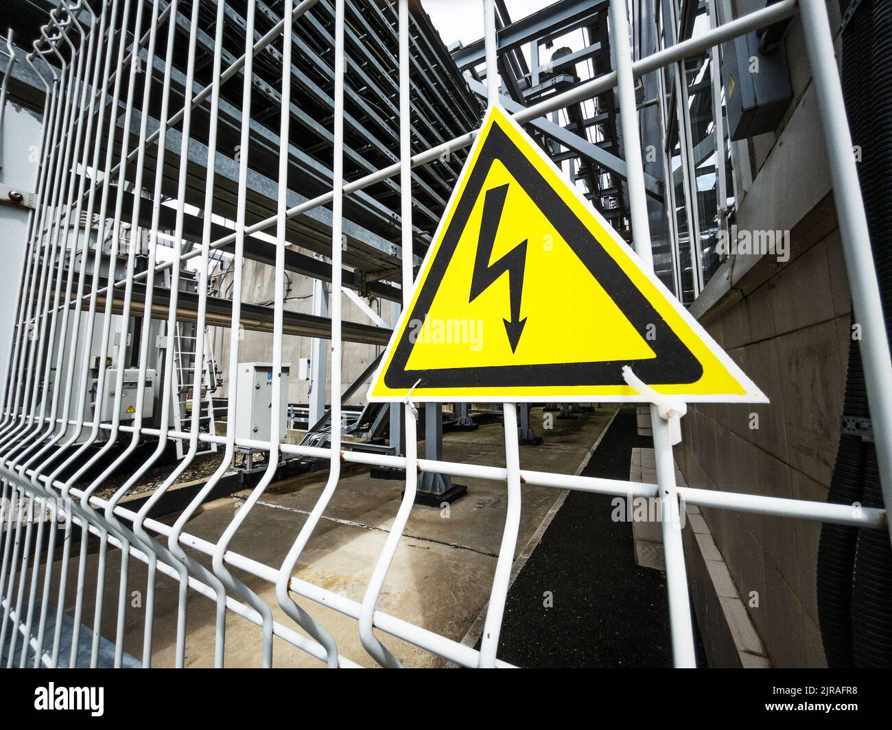 Danger Sign High voltage in the yellow triangle on the metal fence of the grid Stock Photo