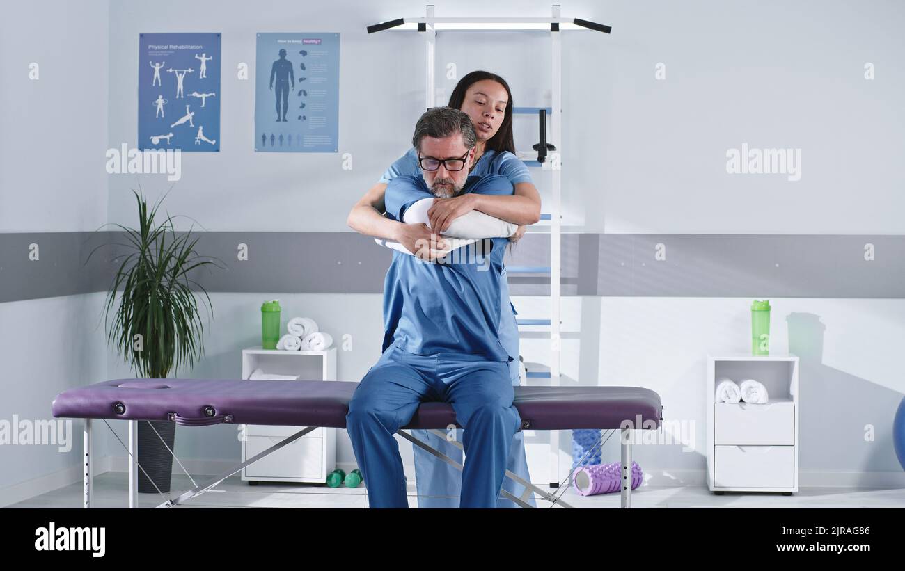 Female doctor stretching arms and shoulders of middle aged man while