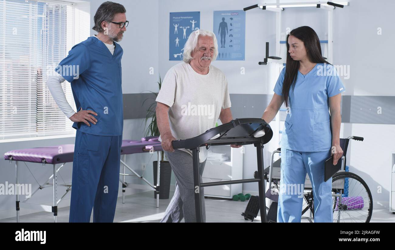 Male and female doctors helping aged man to climb on treadmill and