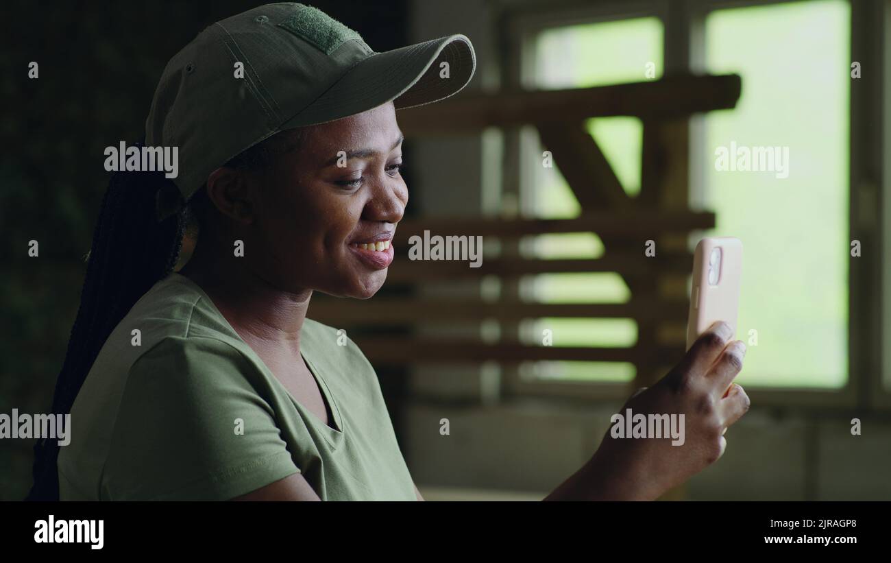 Happy African American female soldier waving hand and smiling while making video call to friend on smartphone Stock Photo