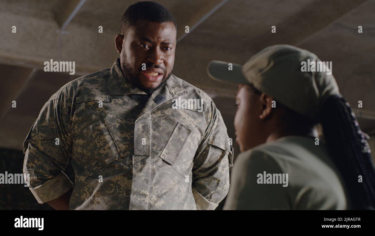 African American commander scolding female soldier under concrete ceiling of military base Stock Photo