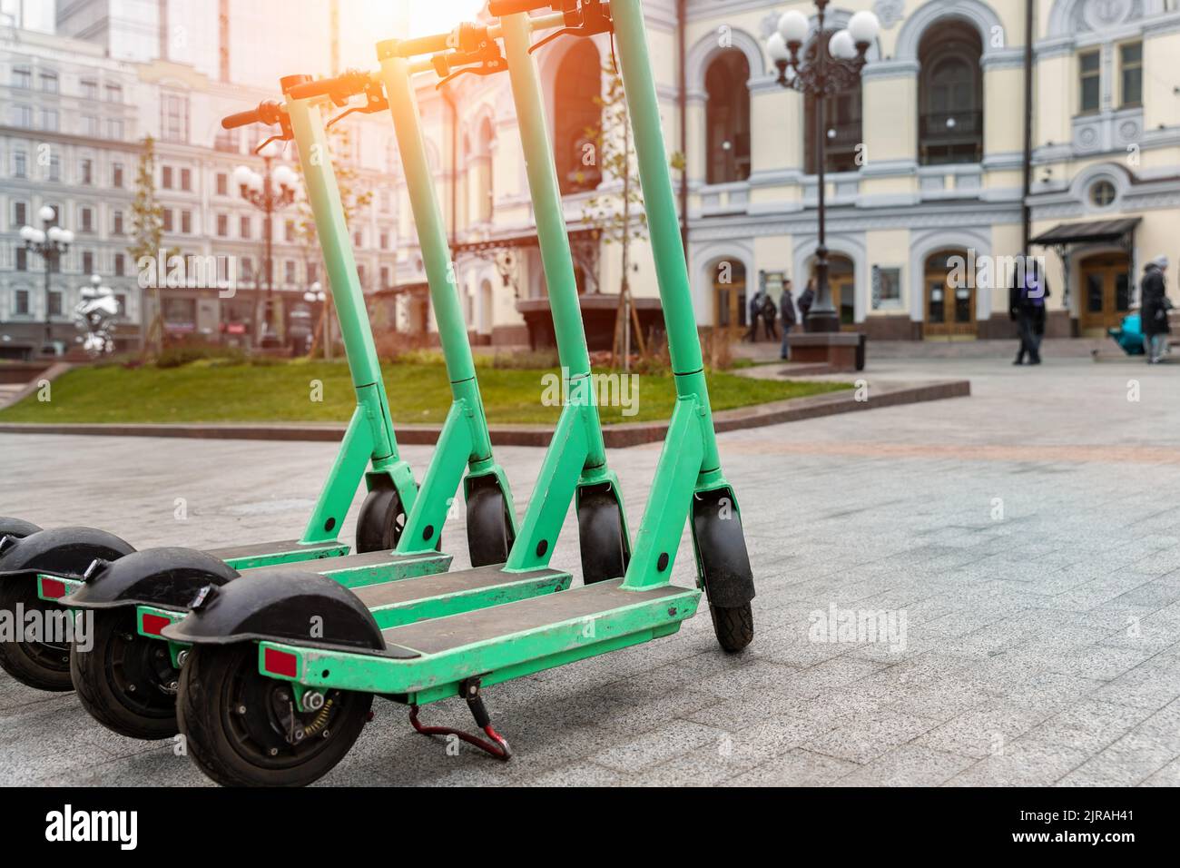 Many modern green electric scooters sharing parked city street. Self