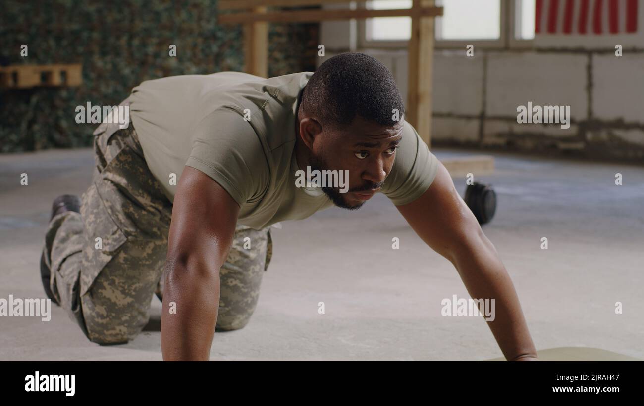 Tired African American male soldier in camouflage doing push ups and taking rest during workout in gym of USA military base Stock Photo