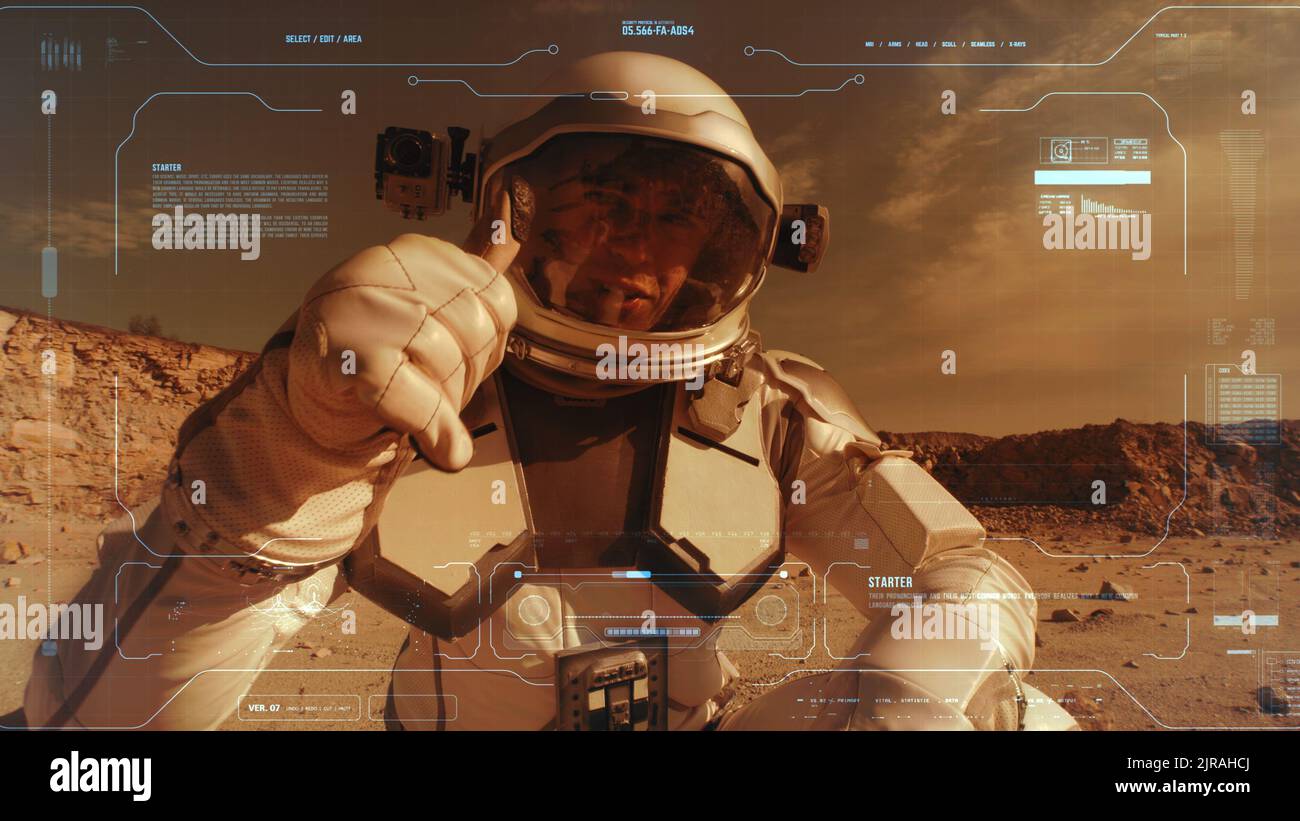 Man in spacesuit turning on camera and pointing at arid terrain while recording video message from surface of Mars Stock Photo