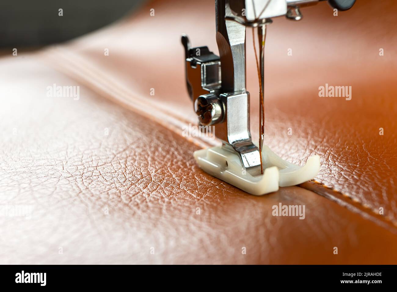 Modern sewing machine presser foot with a needle sews brown leather