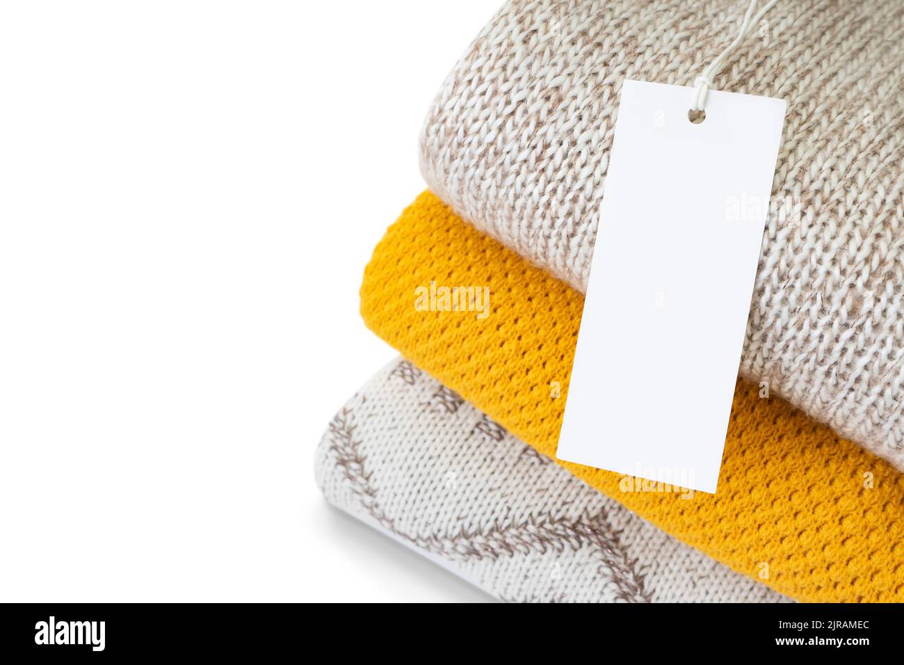 White blank rectangular clothing tag, label mockup template on heap of knitted clothes isolated on white background . Price tag label with copy space Stock Photo