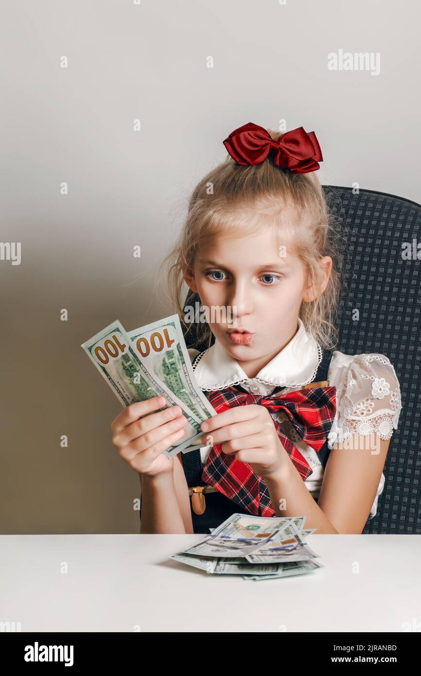 A little girl in a school uniform looks at the money with surprise and