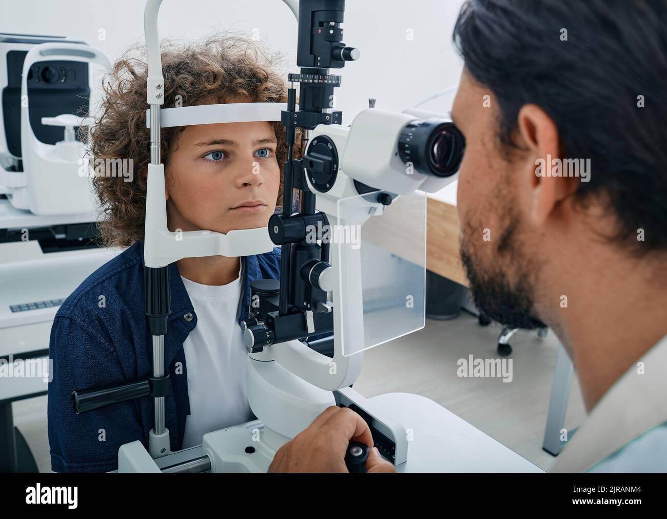 Curly boy getting eye exam at ophthalmology clinic with optometrist
