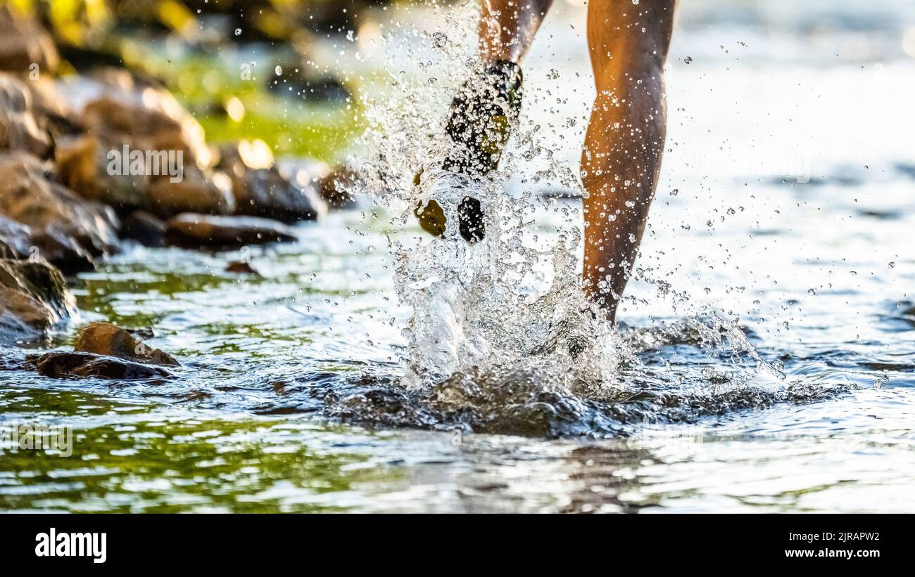 Man running through river splashing water Stock Photo