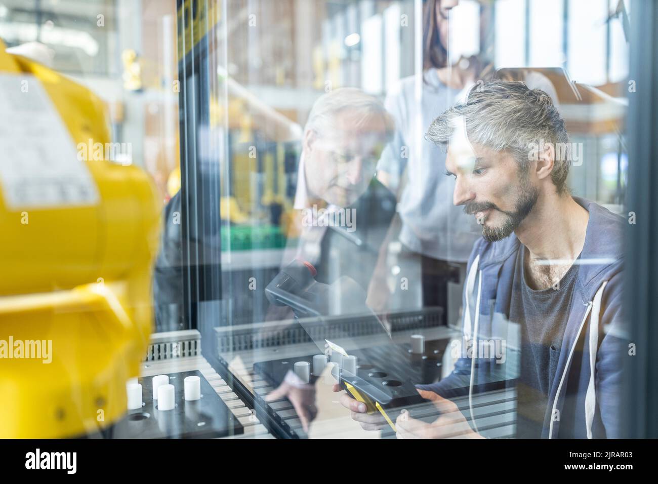Engineers testing industrial robot in glass cabin Stock Photo - Alamy