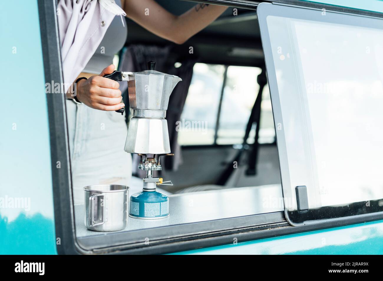 Woman preparing coffee on stove with coffee maker in van Stock Photo