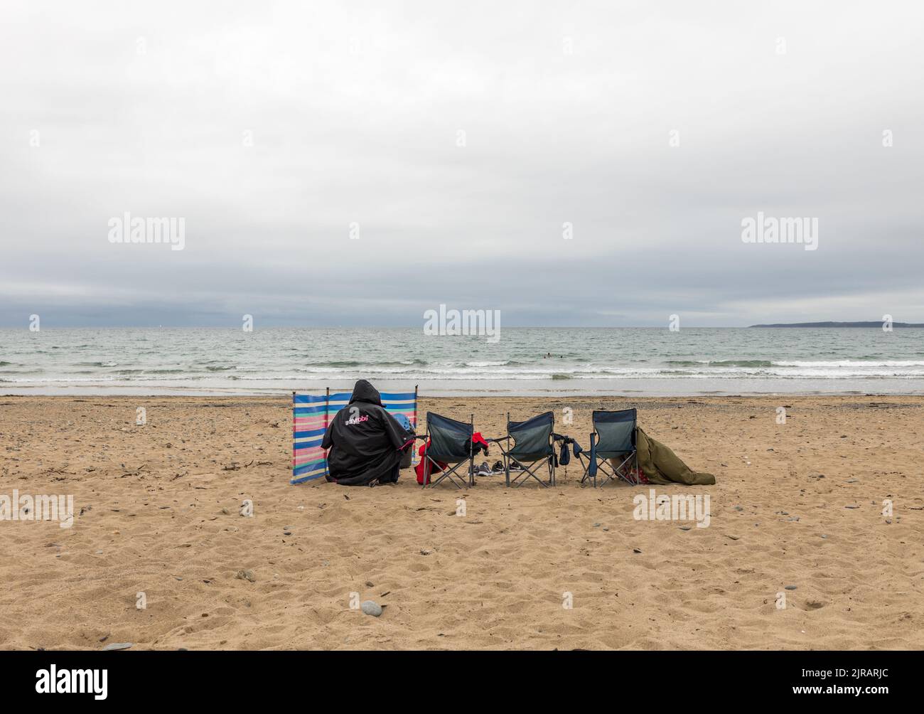 Garrylucas, Cork, Ireland. 23rd August, 2022.  A woman is all wrapped up as she  shelters from the onshore breeze on a deserted beach while watching her family swim at Garrylucas, Co. Cork, Ireland.  - Credit; David Creedon / Alamy Live News Stock Photo