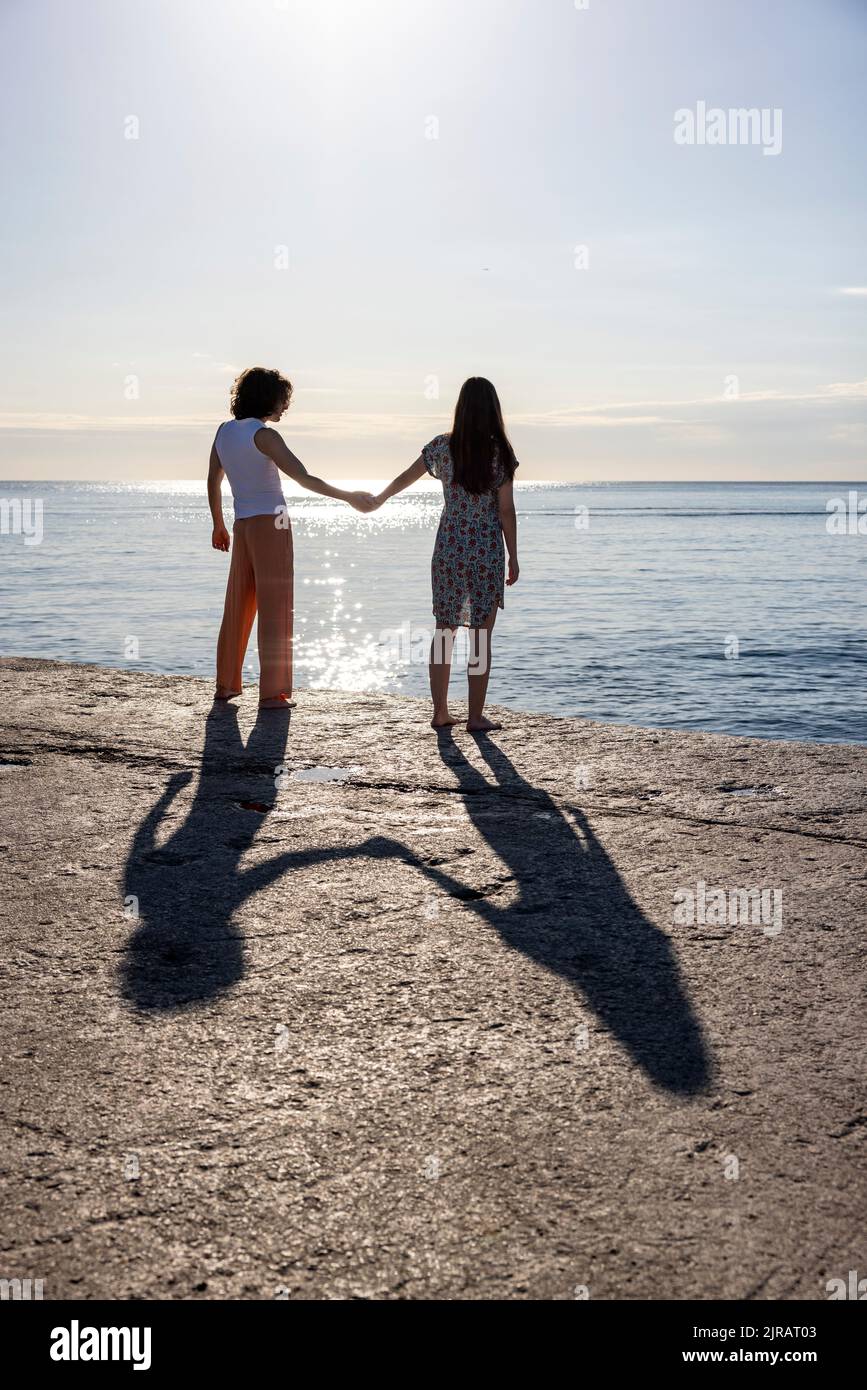 Young couple holding hands on pier looking at sea Stock Photo - Alamy
