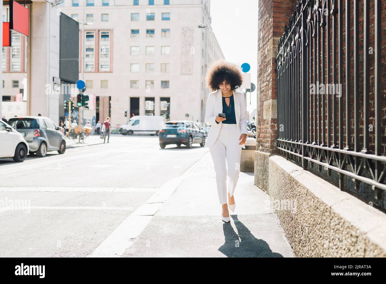 Smiling businesswoman using smart phone walking in city Stock Photo