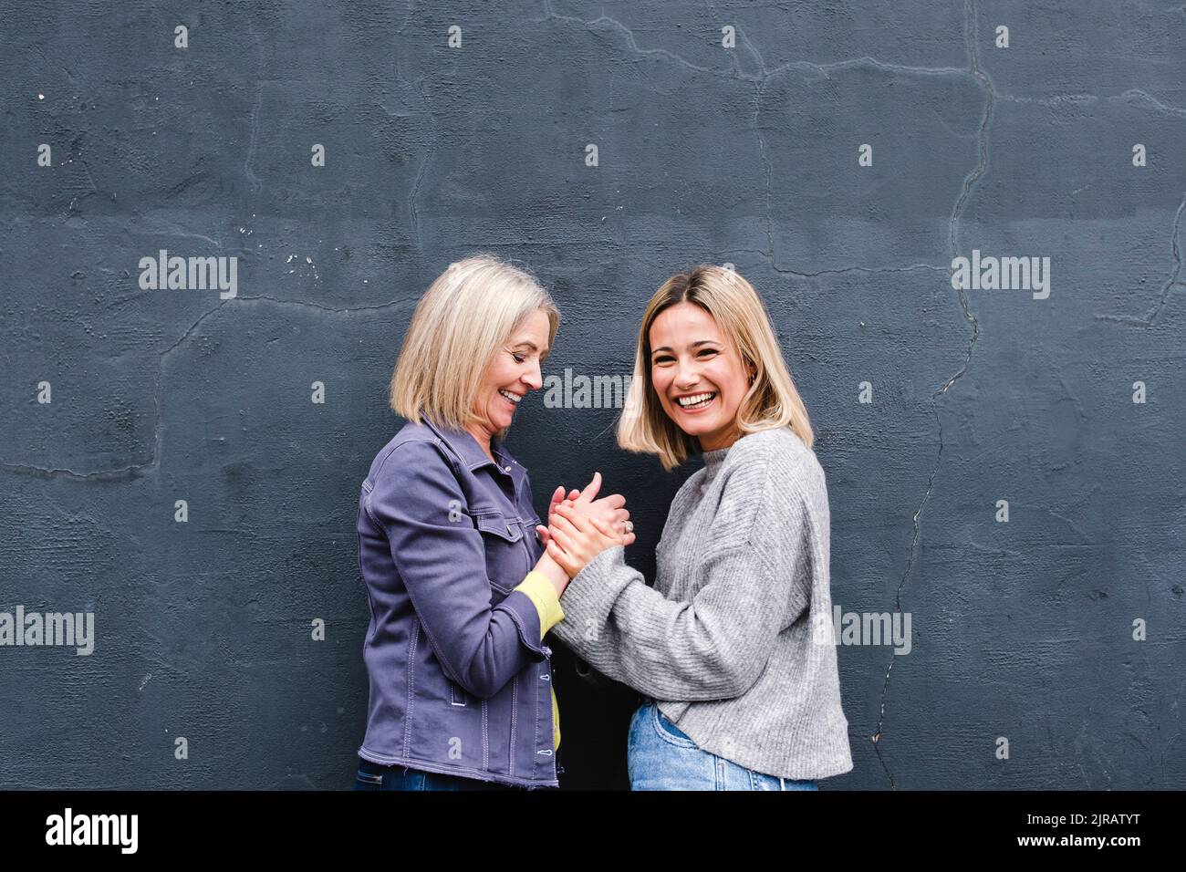 Happy mother and daughter holding hands by wall Stock Photo - Alamy