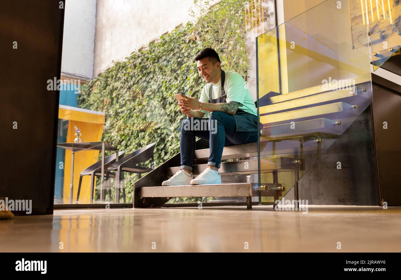 Smiling young man text messaging through smart phone sitting on steps Stock Photo