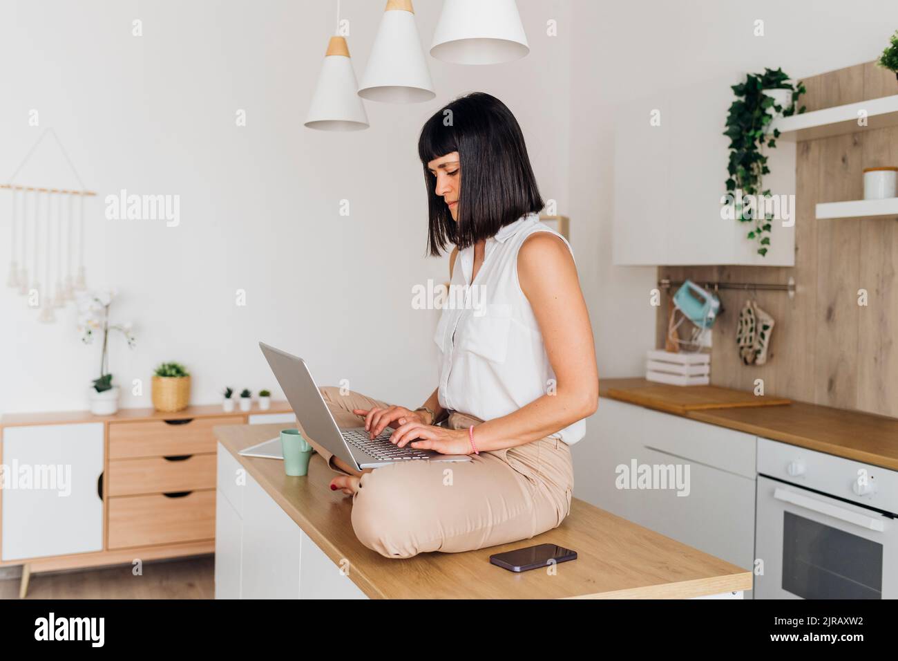 Freelancer sitting on kitchen island with laptop at home Stock Photo