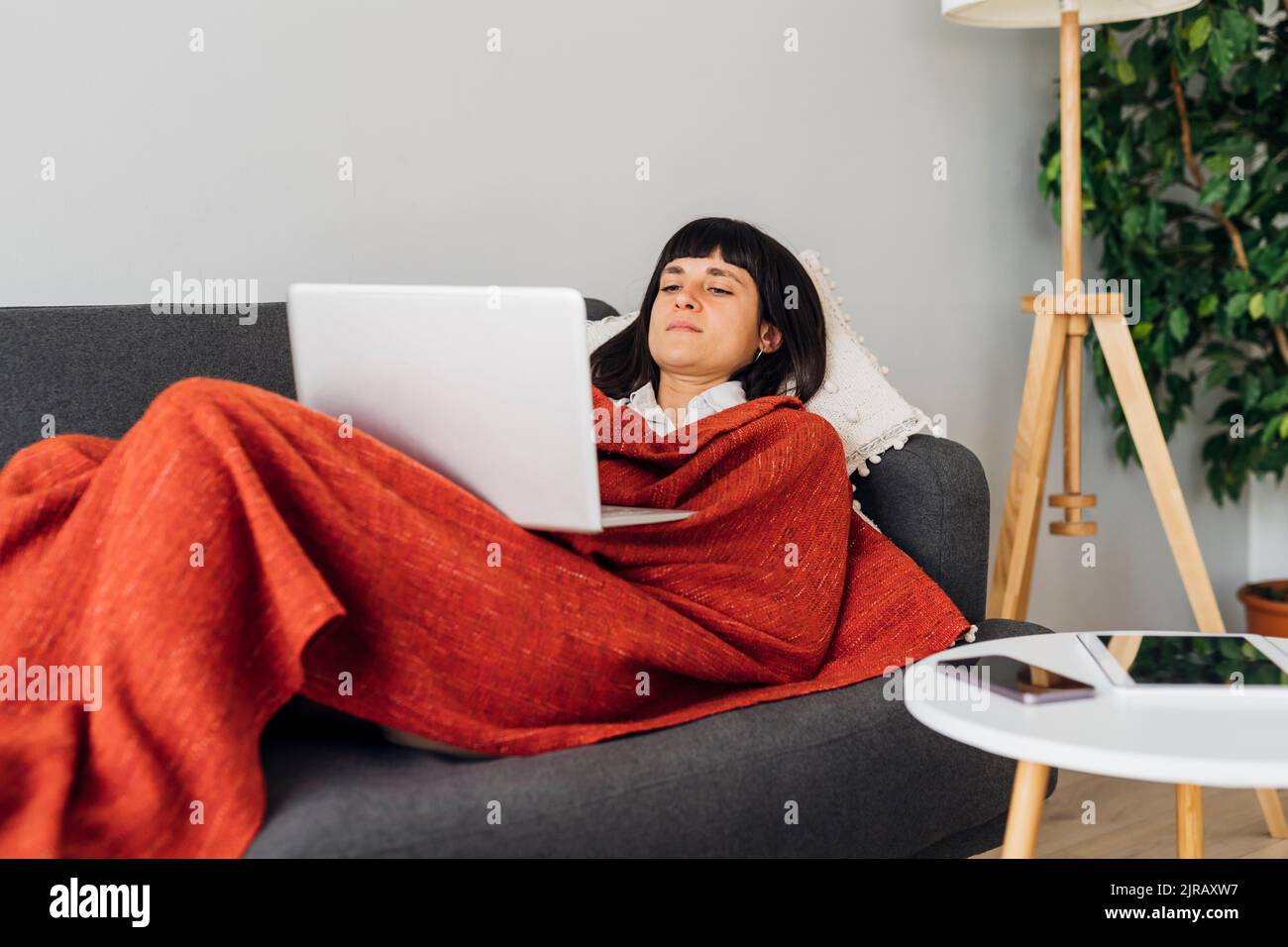 Woman lying on sofa using laptop at home Stock Photo