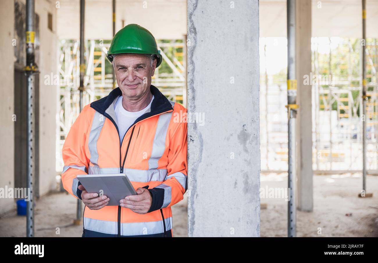 Smiling contractor with tablet PC leaning on column Stock Photo