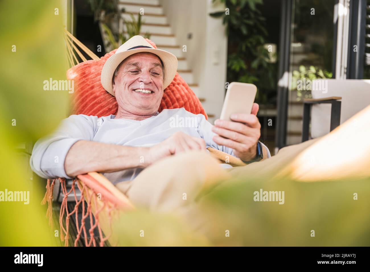 Happy senior man using phone lying in hammock Stock Photo