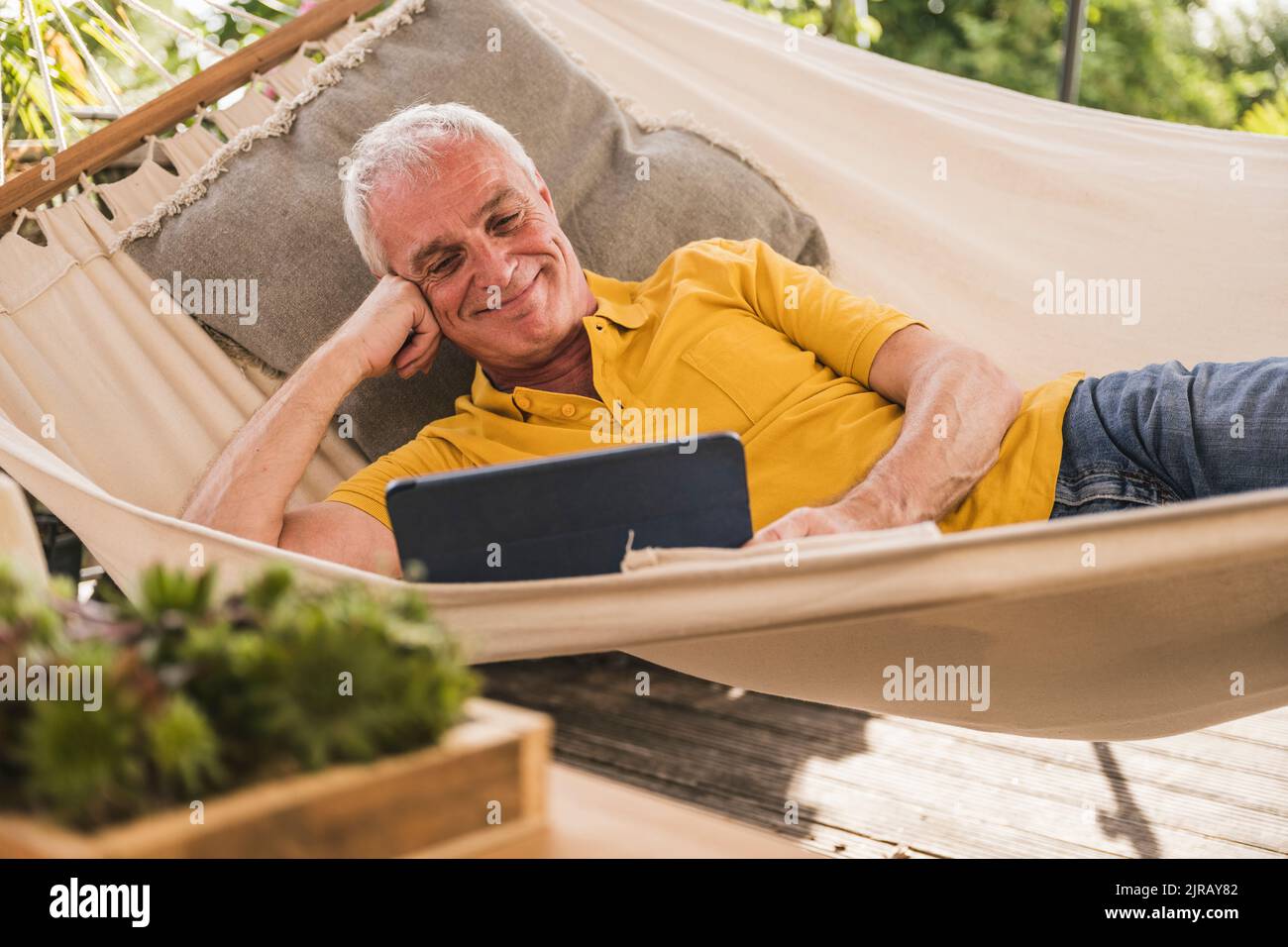 Smiling man using tablet PC lying in hammock Stock Photo