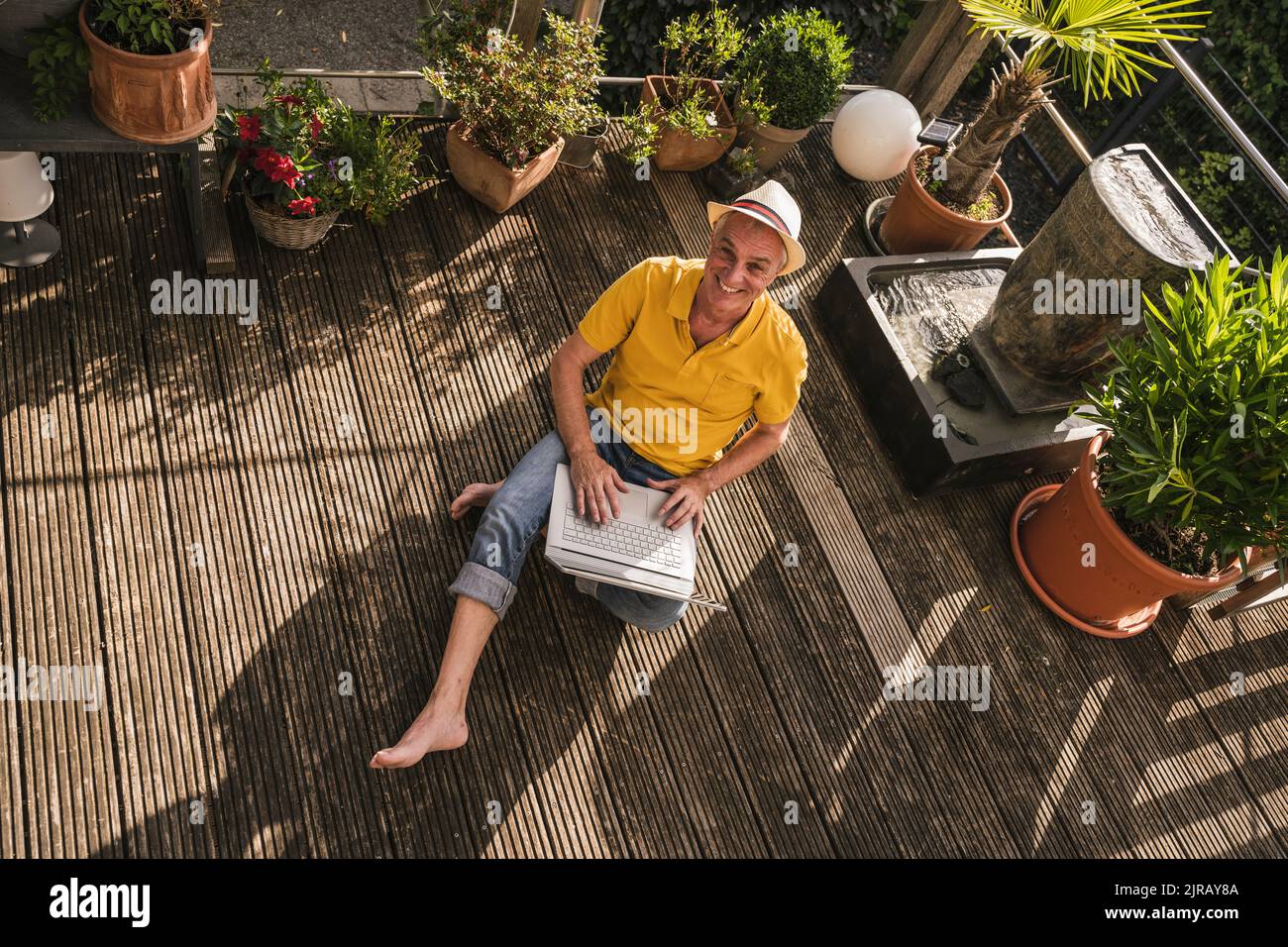Happy man using laptop sitting on terrace Stock Photo