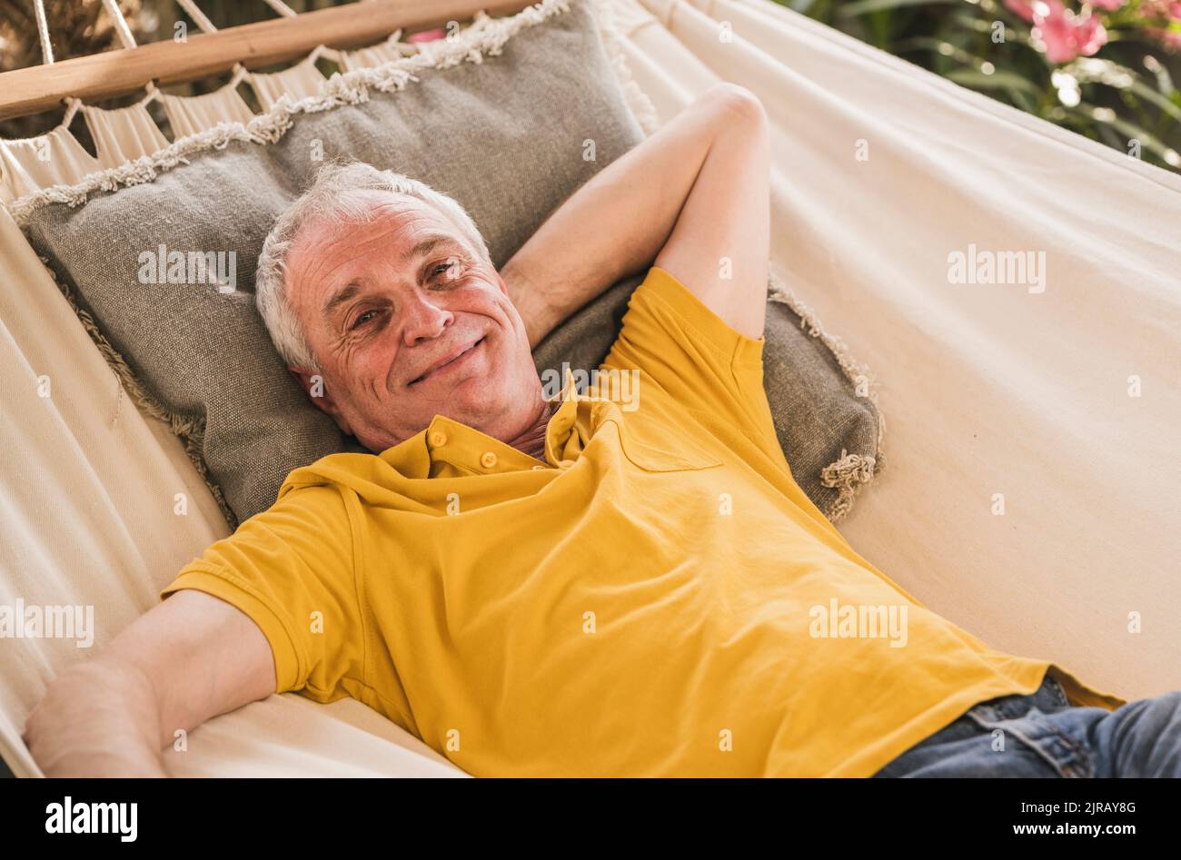Smiling retired senior man with hand behind head relaxing in hammock Stock Photo