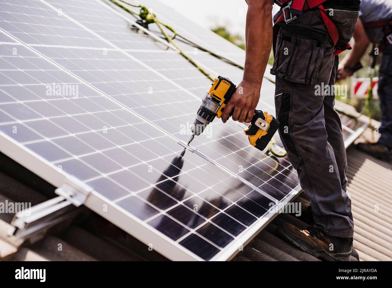 Electrician using power tool for installing solar panel on rooftop