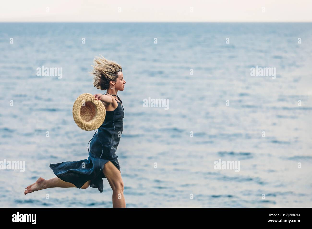Mature woman running with hat in front of sea Stock Photo