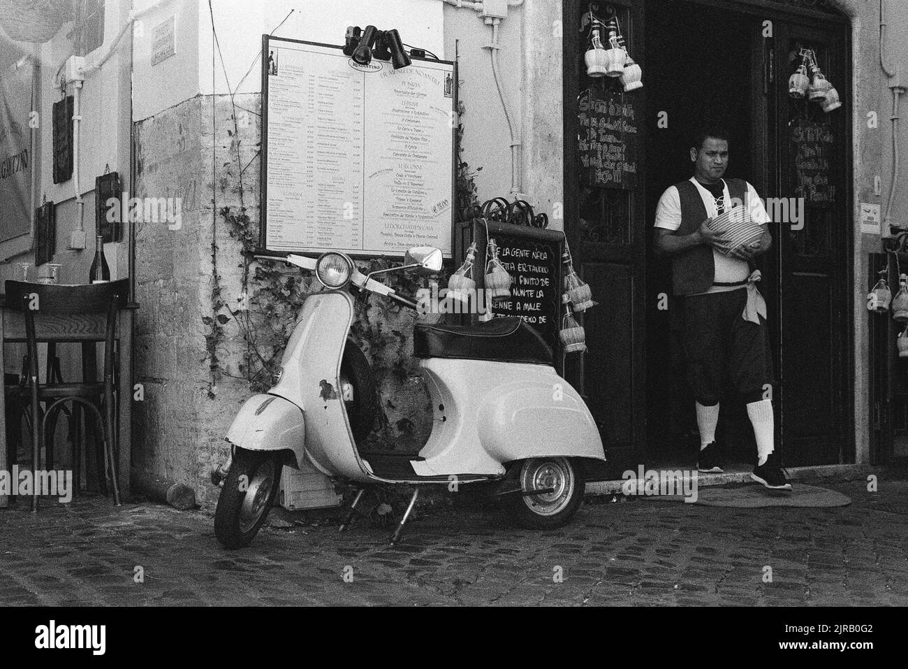 A grayscale shot of Italian Vespa scooter parked in front of a cafe in Rome Stock Photo