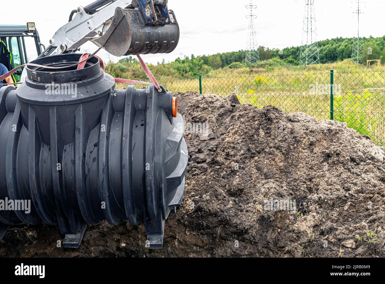 Installation of a single-chamber home sewage treatment plant, the excavator raises the tank. Stock Photo