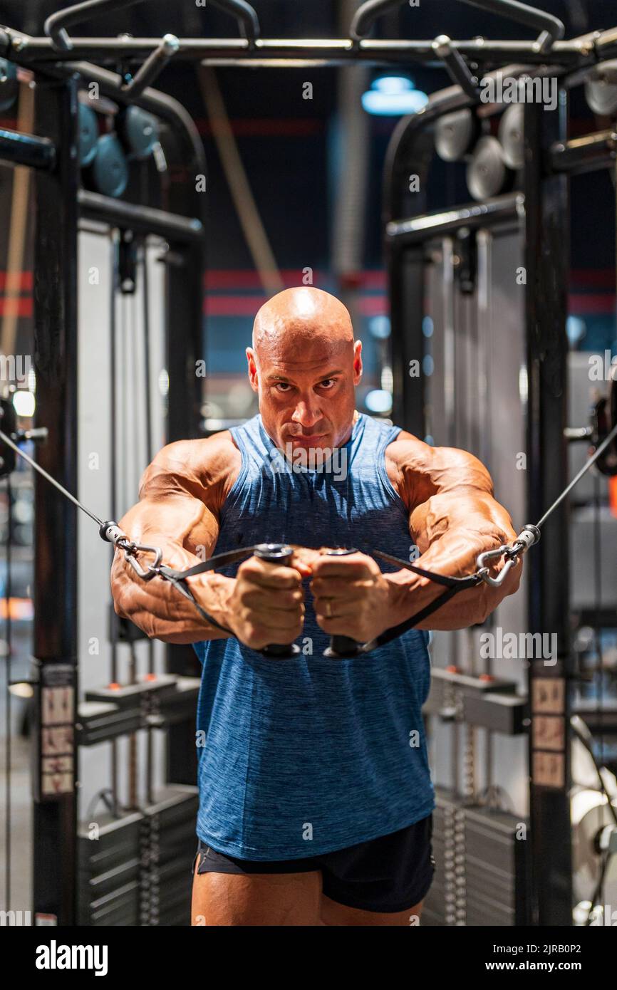 Bald bodybuilder doing chest exercise on cross machine in gym Stock Photo