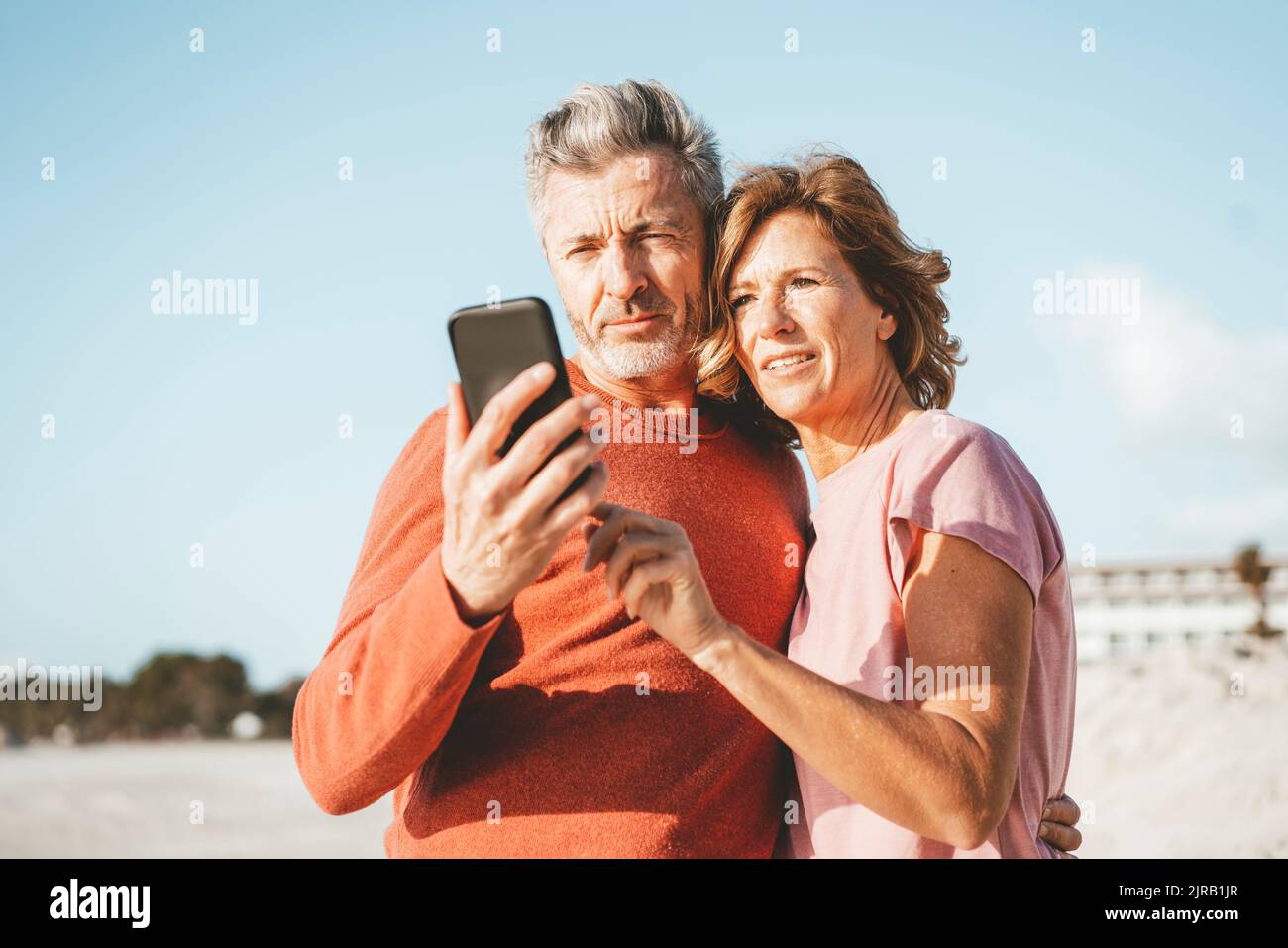 Smiling mature couple using mobile phone at beach Stock Photo