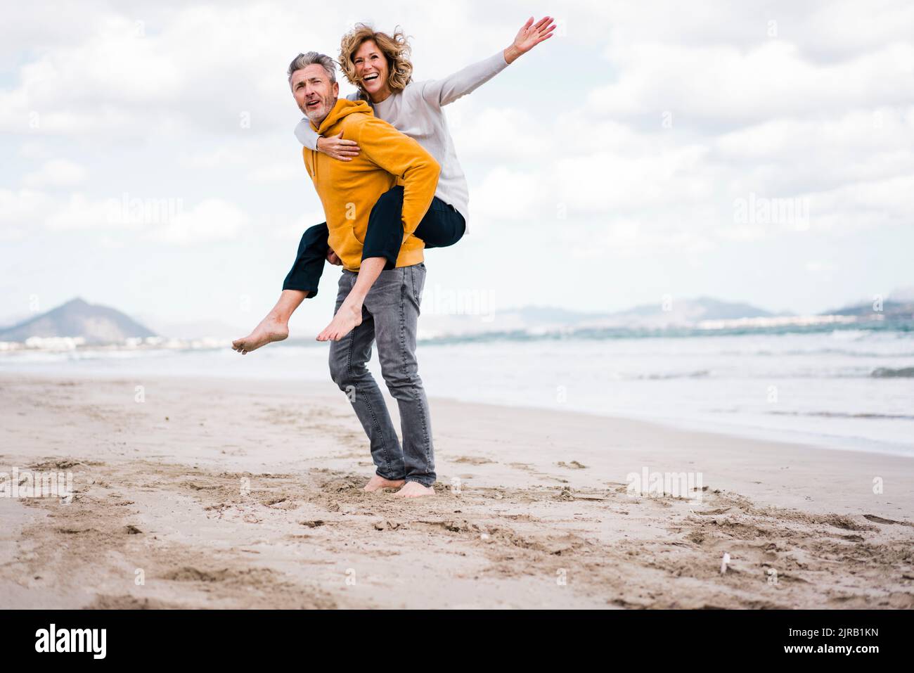 Mature man with woman enjoying piggyback ride at beach Stock Photo - Alamy