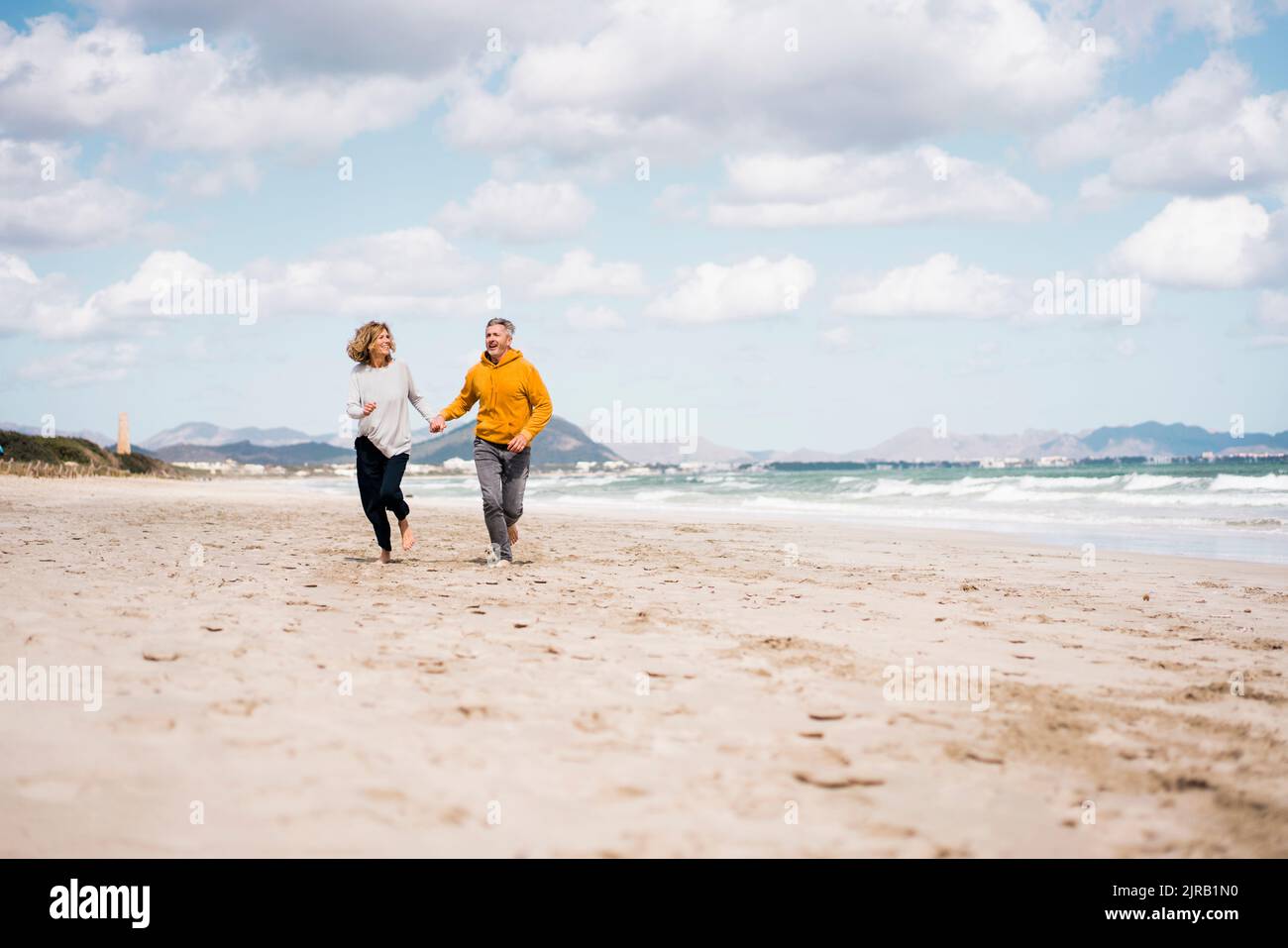 Cheerful mature couple holding hands running on shore at beach Stock ...