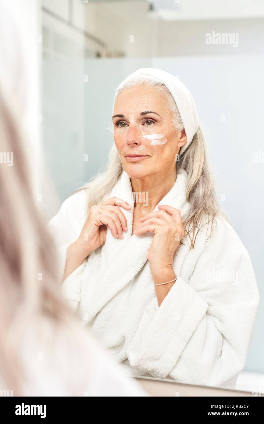 Reflection of woman with cream on face in bathroom Stock Photo