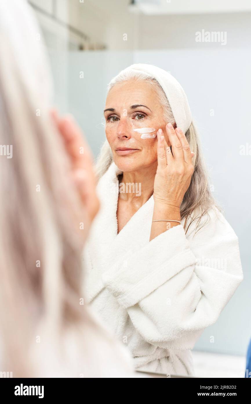 Reflection of woman applying face cream Stock Photo