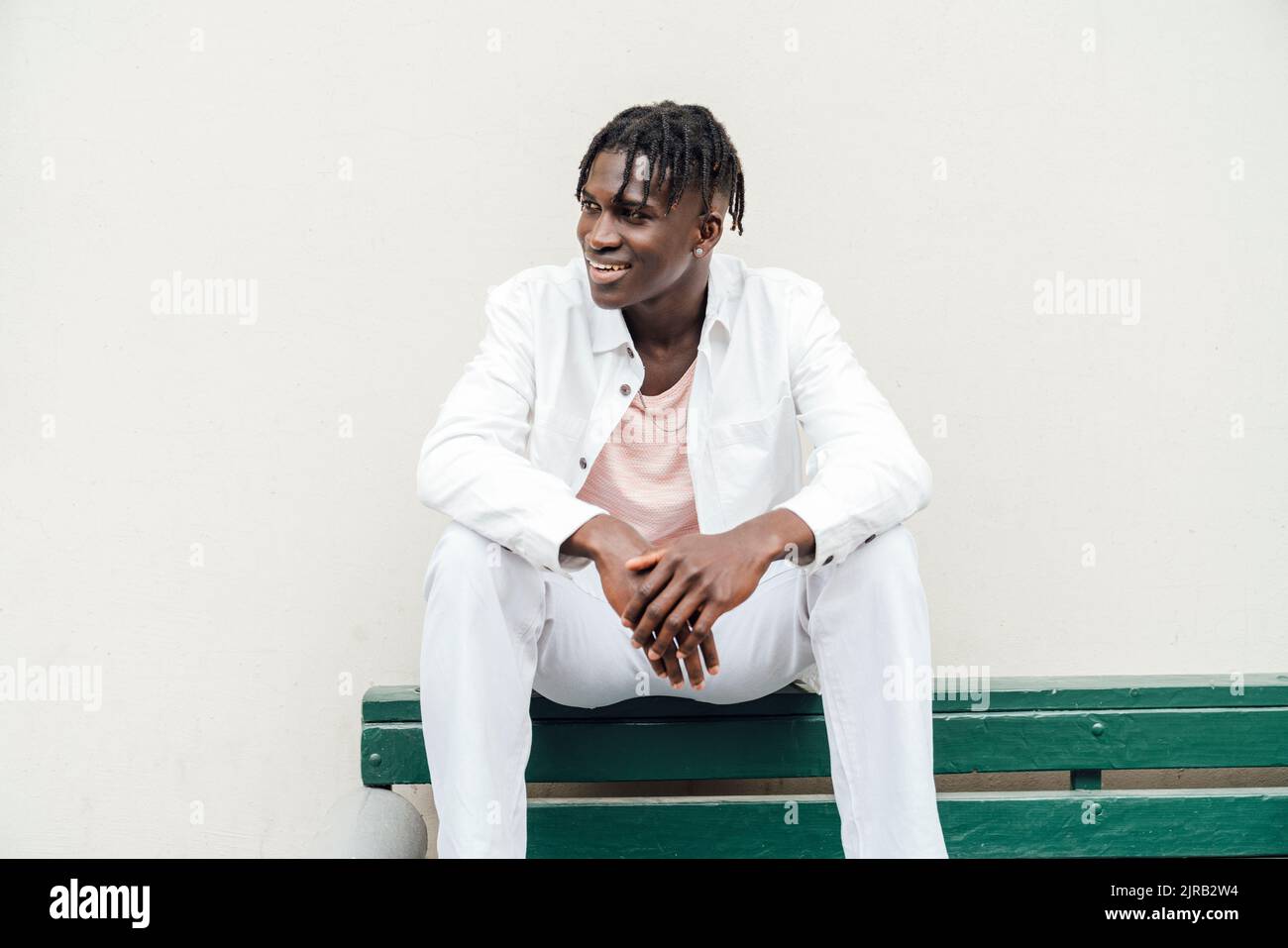Smiling young man with dreadlocks sitting on bench Stock Photo
