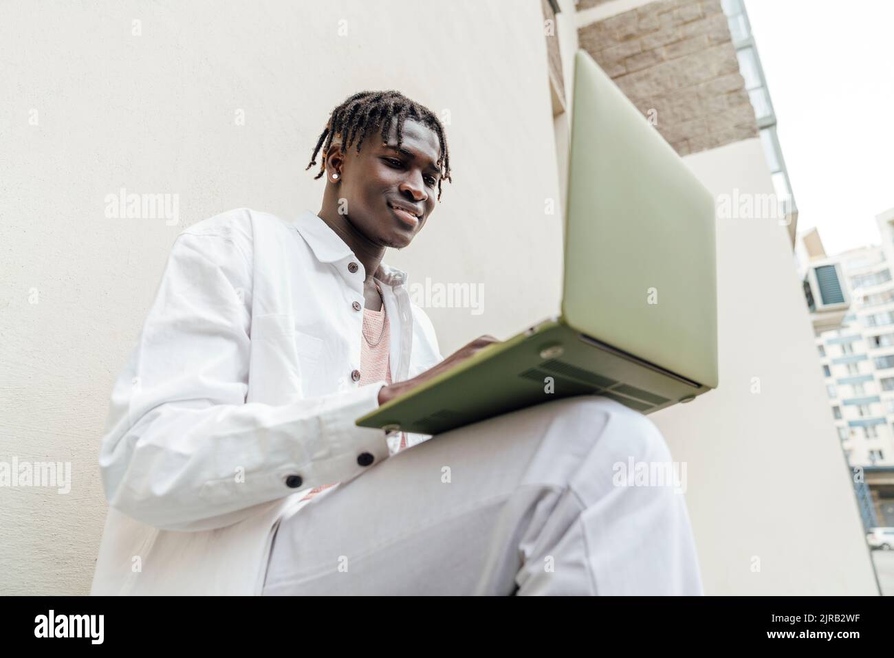 Smiling man using laptop by wall Stock Photo